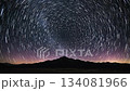 A captivating time lapse shows the night sky adorned with streaking white star trails, rotating above a dark mountain range under a vast celestial expanse. 134081966