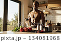 A muscular black man drinks a protein shake in a modern kitchen, surrounded by protein supplements, fresh fruits, and vegetables, emphasizing a healthy and active lifestyle. 134081968