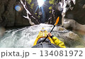 A kayaker navigates a challenging whitewater river in a narrow rocky canyon, captured from a first person perspective with bright sunlight. 134081972