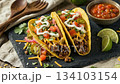 Tasty tacos with spicy beef filling sit on dark background while camera circles around crispy tacos; authentic tacos topped with fresh vegetables make perfect dinner for Mexican cuisine lover 134103154