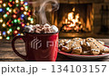 Steaming cup hot chocolate with marshmallows sits near gingerbread cookies while hot chocolate warms up cozy holiday evening; delicious hot chocolate creates festive atmosphere by fireplace 134103157
