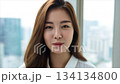 A beautiful Korean woman smiling, with long hair, in an office background with a cityscape_2 134134800