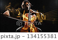 A musician plays the cello in a dim setting. Bright light shapes form around him as he strums the strings, creating a blend of music and visuals. 134155381