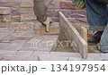 Worker laying paving stones and using a mallet, performing manual labor on a construction site outdoors. 134197954