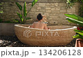 Woman relaxing in outdoor stone bathtub 134206128