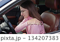 Worried woman sitting in car driver's seat, touching her shoulder in discomfort, experiencing pain while driving. 134207383