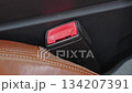 Close-up of a red car seat belt buckle next to brown leather seat, emphasizing safety and protection in vehicle interior design. 134207391