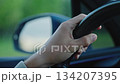 Close-up of male hand on steering wheel while driving, with blurred side mirror and nature background, symbolizing travel, safety, and focus on the road. Road Trip 134207395
