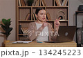 Caucasian woman gesturing emotionally during video conference on laptop. Female frustrated and upset arguing with colleague online sitting at wooden desk in home office with decorative bookshelf. 134245223