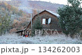 House showcases winter landscape with frost covering ground in morning light. Smoke rises from chimney as people enjoy cold weather surrounded by trees and hills of Ukrainian Carpathians Mountains 134262003
