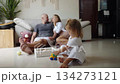 Little girl plays with a toy on the floor while her parents sit behind her 134273121