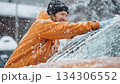 Smiling man cleaning car windshield during heavy snowfall in winter 134306552