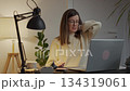 Woman sitting at a home desk holding his neck, suffering from pain while working on a laptop. Concept of ergonomic posture and discomfort due to working on computer 134319061