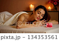 Young beautiful woman relaxing on a massage table in a spa center. Serene atmosphere with candlelight for ultimate relaxation and wellness 134353561
