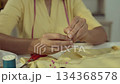 Asian woman threading the needle. Tailor working in her studio with focus in hands putting thread in sewing needle. 134368578