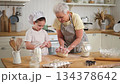 Happy family in kitchen. Grandmother and granddaughter child cook in kitchen together. Grandma teaching kid girl knead dough bake cookies. Household teamwork helping family generations concept 134378642