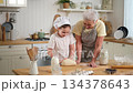 Happy family in kitchen. Grandmother and granddaughter child cook in kitchen together. Grandma teaching kid girl knead dough bake cookies. Household teamwork helping family generations concept 134378643