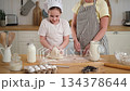 Happy family in kitchen. Grandmother and granddaughter child cook in kitchen together. Grandma teaching kid girl knead dough bake cookies. Household teamwork helping family generations concept 134378644