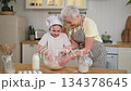 Happy family in kitchen. Grandmother and granddaughter child cook in kitchen together. Grandma teaching kid girl knead dough bake cookies. Household teamwork helping family generations concept 134378645