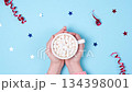 Camera slowly pulls away from hands holding a mug of hot chocolate with marshmallows, surrounded by festive stars and ribbons on a bright blue background 134398001