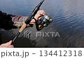 Fisherman catching fish, pulling rod while fishing from lake or pond outdoors. Hands of unrecognizable man spins a spinning reel on the river bank. Fishing for pike, and perch. Fishing day concept 134412318