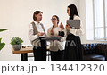 Three professional businesswomen with laptop discussing campaign new ideas, work project, business solutions in modern office, near the desk and large window. Teamwork, communication, collaboration 134412320