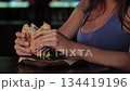 Young beautiful redhead girl holding tasty beef burger with two hands over the table. Eating tasty food at home. Close-up high quality 4k footage 134419196