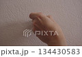 Hand peeling protective film from double-sided adhesive tape on wallpapered wall, getting ready for mounting, fixing or attaching items without drilling, closeup, unrecognizable person, slow motion. 134430583