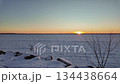 Serene winter landscape with snow-covered rocks and trees, as sun rises over frozen lake, showcasing gradual light change and color transition 134438664