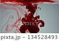 Red ink or paint dispersing and swirling in clear water creating abstract fluid motion patterns 134528493