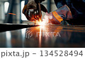 Professional welder creating bright orange sparks while welding metal in industrial workshop factory setting 134528494