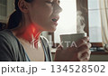 Young European woman experiencing severe sore throat pain while drinking hot tea in bright modern kitchen during morning 134528502