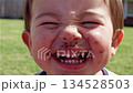 Young European boy with dirty face laughing hysterically outdoors with chocolate or mud covered cheeks and bright smile in sunny backyard 134528503