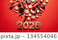 Vibrant arrangement of makeup products and gold numbers 2026 on a bold red background, showcasing beauty essentials in a dynamic visual flow 134554046