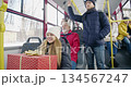 Side view of passengers traveling by bus. Small girl holding gift box, smiling, old man wearing red jacket, sitting, boy standing, handle holding. Concept of public transport. 134567247