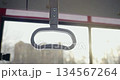 Front view of grey bus handle on empty bus. Bus topping with handle for holding, panorama os sunny evening city on background. Concept of public transport and urban settings, 134567264