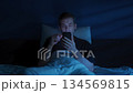 Frustrated man lies awake at night, doom scrolling social media or news feed 134569815
