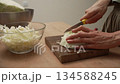 Close-up shot of a chef expertly slicing a crisp white cabbage on a wooden cutting board, carefully preparing the raw vegetable for a nutritious salad in a cozy home kitchen setting 134588245