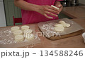Skilled hands of a woman shaping classic cottage cheese pancakes, also known as syrniki, on a dusted countertop in a cozy kitchen before gently transferring the dough onto parchment paper for baking 134588246