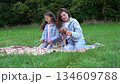 Happy family having picnic in the park enjoying summer and nature cheerful mom cuddling her little daughter and their dog on the green grass during funny outdoor rest 134609788