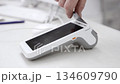 Pay by phone on electronic payment machine or card reader. E-money at cashless wallet. Female hand with pos-terminal and cellphone closeup. Client pays for the procedure in modern beauty clinic. 134609790