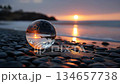 Sunset Reflected in Glass Sphere on Rocky Shore 134657738
