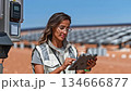 A female engineer checks an inverter station, compares data on a tablet, renewable energy sources 134666877