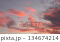 A plane flies through a colorful sky filled with pink and gray clouds during sunset. The scene captures the beauty of aviation and nature. 134674214