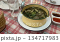 A clear herbal soup with vegetables and meat sits in a small enamel pot. The dish is served hot as a shared meal on a dining table. 134717983