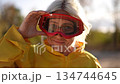 Relaxed woman wearing red goggles adjusting yellow jacket during golden hour 134744645