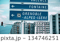 Road signs pointing to Grenoble Alpes Isere airport with alpine mountains and urban buildings 134746251