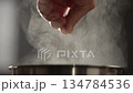 Slow motion man adding salt to boiling water in saucepan with strong backlight 134784536