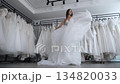 A beautiful, slim bride with flowing locks is twirling in a wedding gown in a wedding boutique, a woman is trying on. Time-lapse. Stabilized camera view from below. A wedding boutique.  134820033