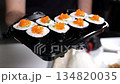 Close-up of a chef wearing gloves holding a disposable plate with sliced sushi with red caviar. Japanese restaurant, takeout and delivery. 134820035